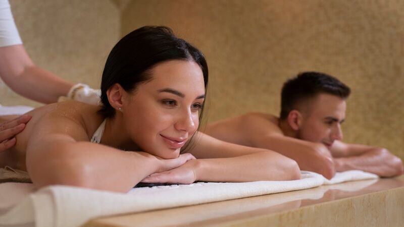 A smiling woman and a man lying on side-by-side massage tables during a couples massage