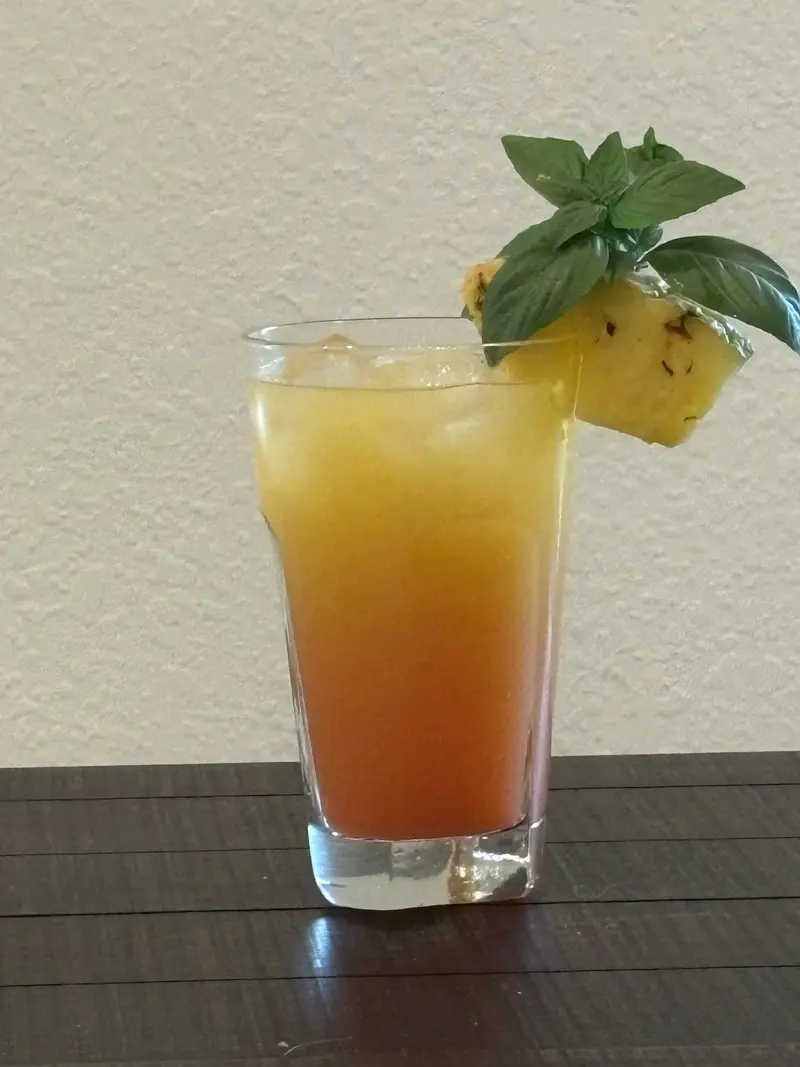 Hawaiian Sunset drink with an amber sunset color, garnished with a pineapple wedge and fresh basil.